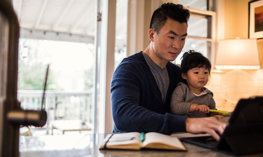 man with young son on his lap sitting at home an working on E-learning